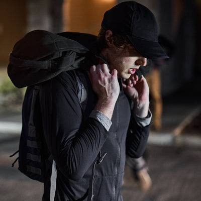 A person wearing a Performance Running Hat - ToughMesh, crafted from premium Italian fabric, carries a backpack on their shoulder as they walk at night.