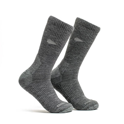 A pair of Merino Challenge Socks - Crew by GORUCK, featuring a gray ribbed design with reinforced heels and toes, stand upright on a white background. These boot-height socks offer a subtle texture and display a small logo near the top, all supported by the Scars Lifetime Guarantee for enduring quality.