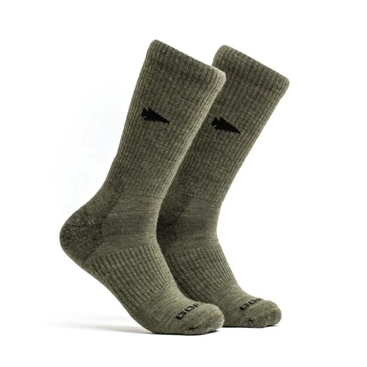 A pair of tall, green Merino Challenge Socks - Crew by GORUCK with black logo embroidery near the top. They feature a ribbed texture and display the GORUCK brand name on the toe area. Positioned upright, slightly angled to the side, these boot height socks come with a Scars Lifetime Guarantee for lasting wear.