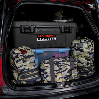 In the car trunk, camo bags were placed beside a container marked "Prohibited Reptile," and in the corner was a GORUCK Bullet Ruck Classic - Cordura, featuring a streamlined design and padded straps.