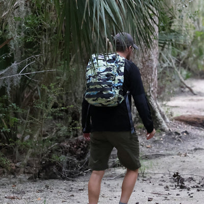 A person is hiking on a forest trail, wearing the GR1 USA - Cordura (The Original Ruck) backpack by GORUCK, reminiscent of the Special Forces' robust gear, and a cap.