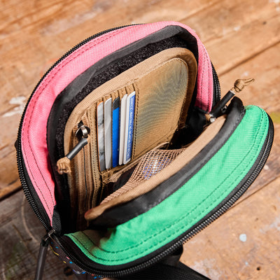 An open Admin Panels wallet from GORUCK, placed on a wooden surface, exhibits an array of credit cards and compartments. This vibrant accessory, featuring pink and green fabric, is perfect for everyday carry (EDC). Its zip closure ensures everything stays secure, making it ideal for travel adventures.