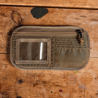 The "Admin Panels" by GORUCK, an ideal EDC accessory, boasts a zipper compartment and a clear ID pouch. It rests on a rustic wooden surface with visible scratches and paint marks.