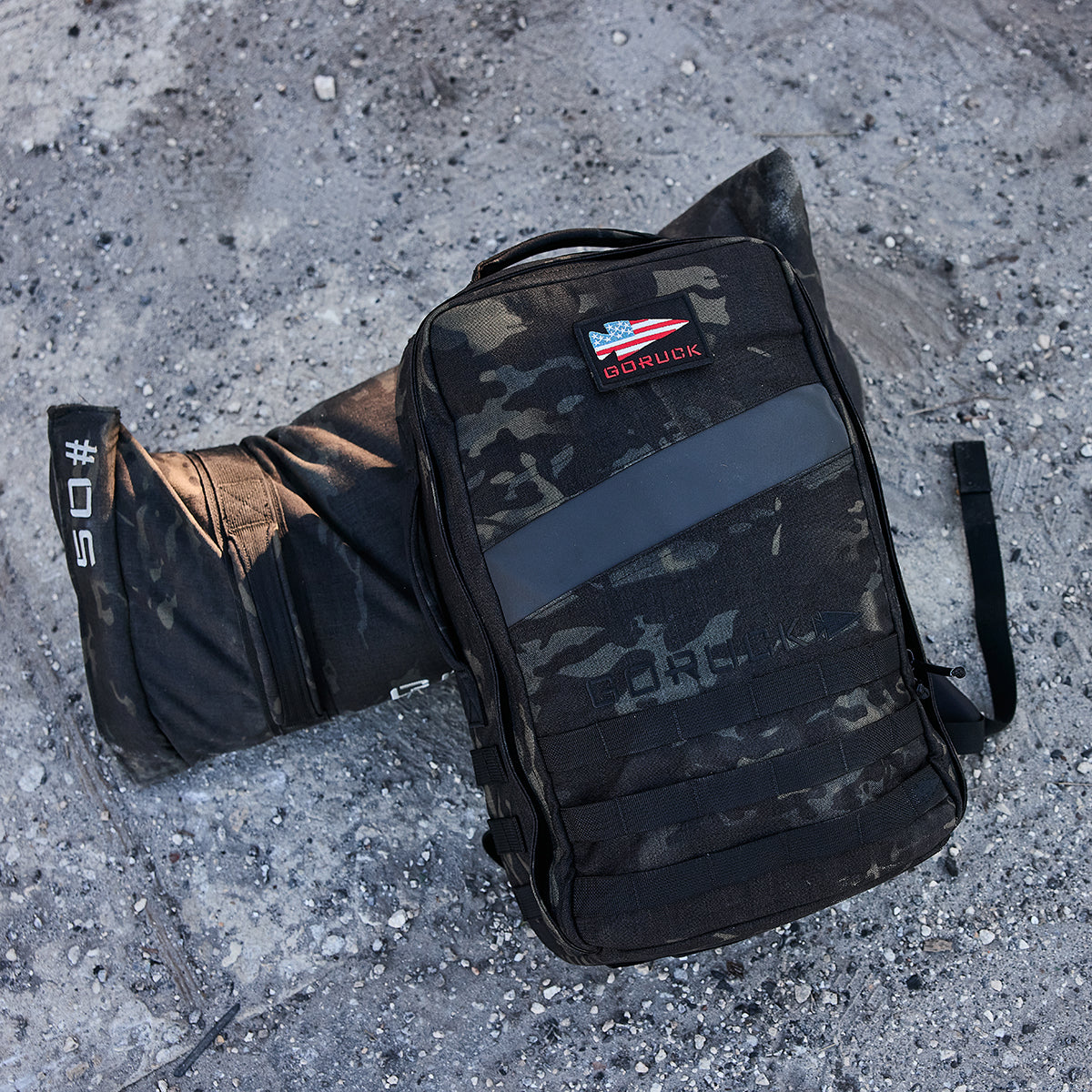 A black Rucker 4.0 and a sandbag rest on the gravel surface.