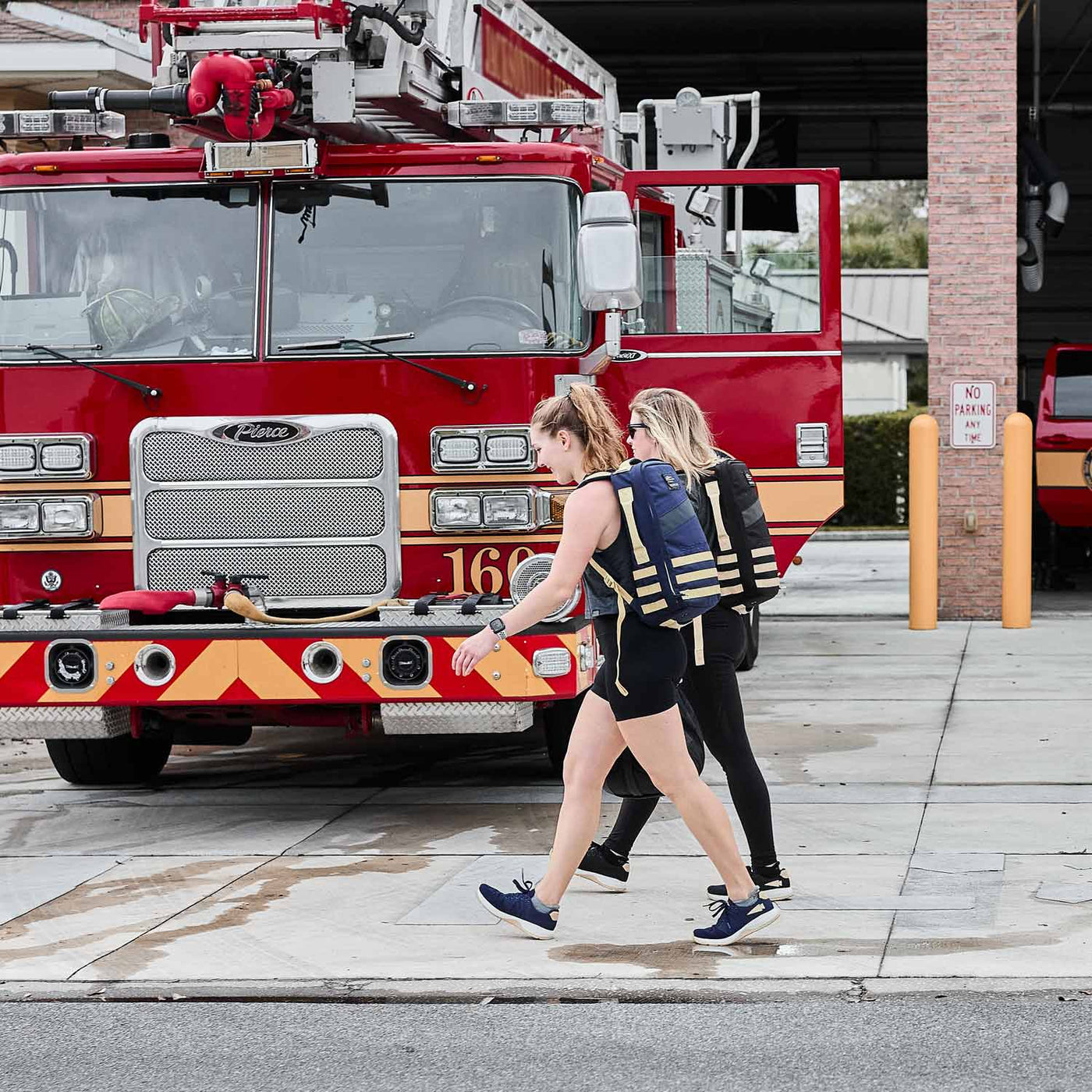 Two women walk past a fire truck, one carrying a large backpack made from CORDURA® Ballistic Nylon by GORUCK.