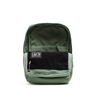 The KR1 2.0 - Kid Ruck by GORUCK is a green kids backpack featuring a black front pocket, shown open to reveal its interior against a white background. Designed for durability with reinforced stitching, this pack is ready for any adventure.