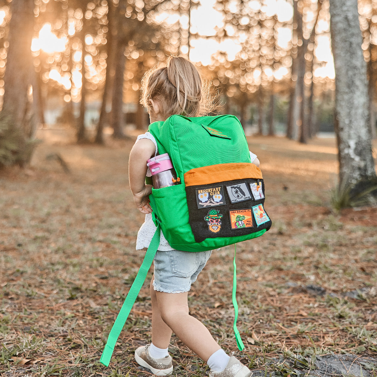 A child wanders through the sunlit forest, proudly wearing the KR1 2.0 - Kid Ruck from GORUCK. Its rugged pack design and reinforced stitching ensure a day full of endless adventure.