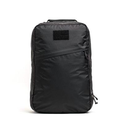 Introducing the GR1 USA - X-PAC rucksack by GORUCK, a sleek black bag with a rectangular design. It features a subtle diagonal seam and a small patch at the top, crafted from waterproof X-PAC material. The rucksack includes a side zippered closure and a convenient top handle for easy carrying.