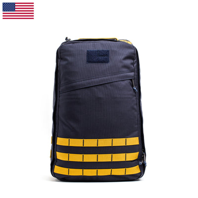 The GR1 USA - Cordura (The Original Ruck) in dark gray, featuring yellow webbing straps and displayed next to a small American flag icon, captures the essence of a GORUCK Challenge inspired by Special Forces.