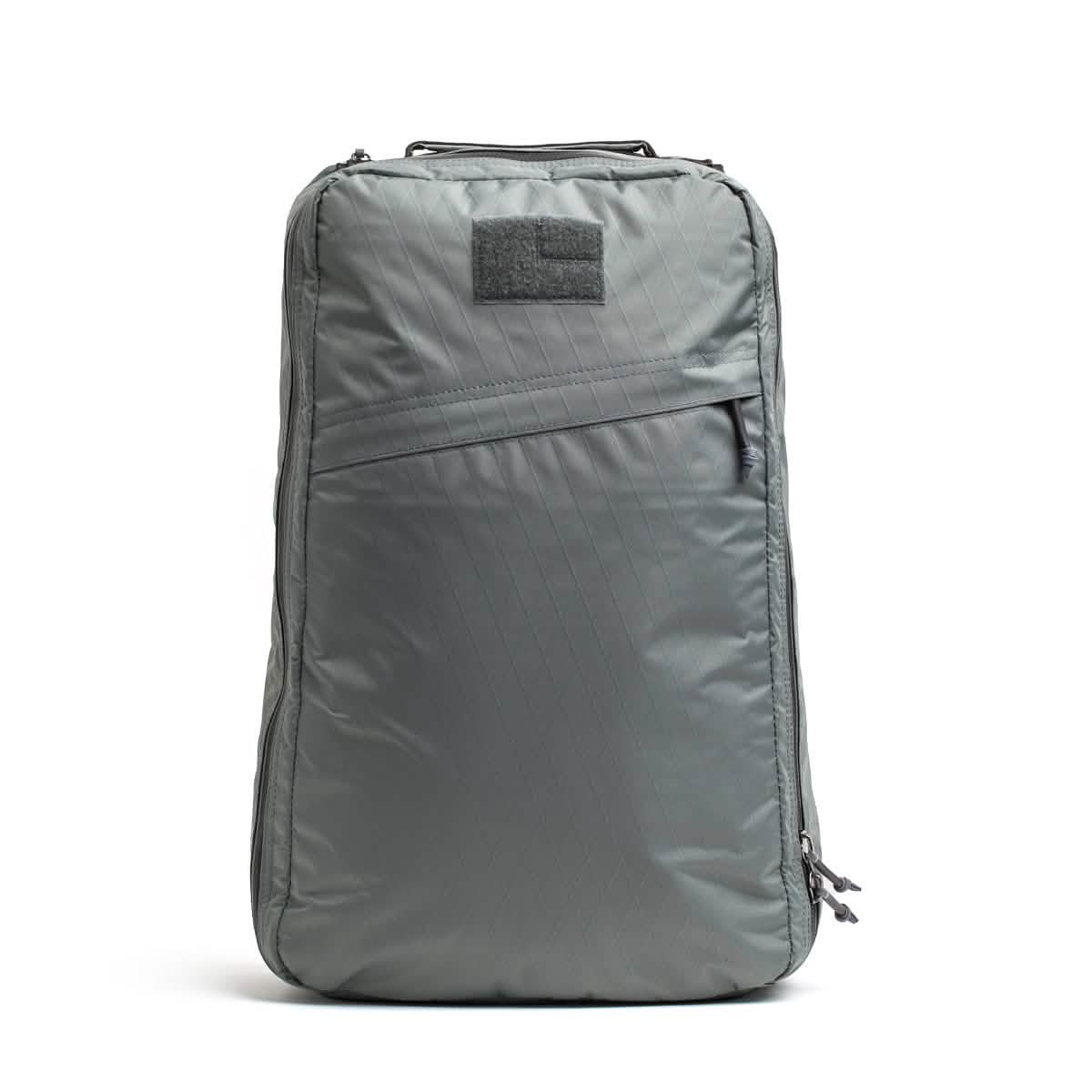 The GORUCK GR1 USA - X-PAC is a sleek, gray rucksack boasting a minimalist design. Constructed from durable X-PAC fabric, it offers weather resistance and waterproof qualities. It includes a top handle, front zippered pocket, and main compartment, all highlighted by a subtle patch near the top.