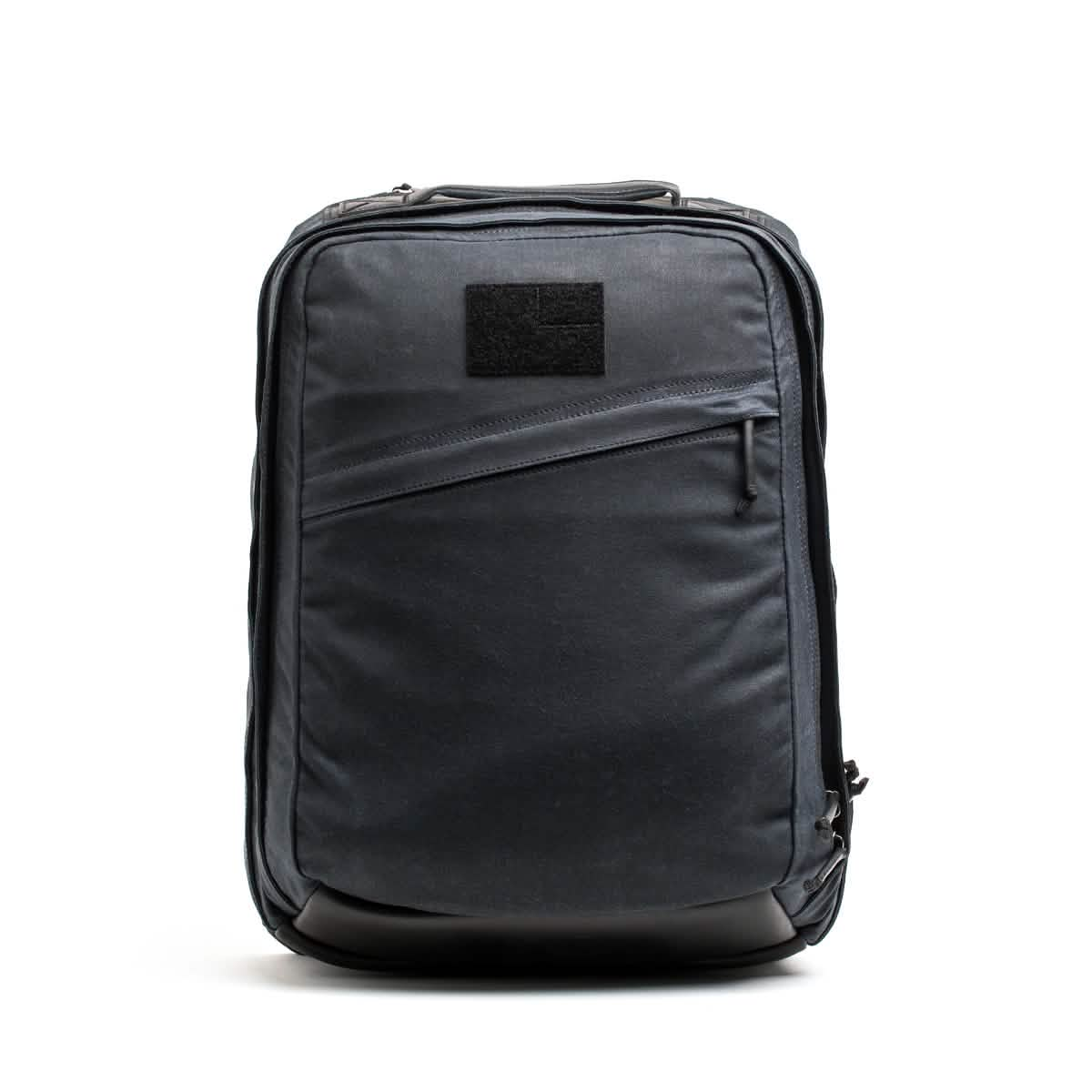 Introducing the GR2 - Waxed Canvas backpack by GORUCK: a sleek, modern black accessory crafted from durable waxed duck canvas. It features a diagonal front zipper pocket and a rectangular patch near the top, enhancing its minimalist design. The smooth fabric and subtle detailing contribute to its refined aesthetic. Photographed against a plain white background, this backpack exudes a touch of heritage retro rucksack style.