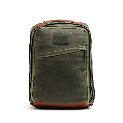 Introducing the GR2 - Waxed Canvas by GORUCK: a green backpack designed in a classic, rectangular shape reminiscent of a Heritage Retro Rucksack. It features Red Wing Leather accents on the top and bottom and includes a front zippered pocket for added utility. With a loop handle, this rugged and functional backpack is ideal for modern adventurers.