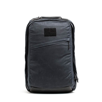 Introducing the GORUCK GR2 - Waxed Canvas, a sleek black backpack crafted from waxed duck canvas for a smooth texture and structured shape. It features a front zipper pocket and a rectangular patch near the top, making it an ideal choice for travel or everyday use.