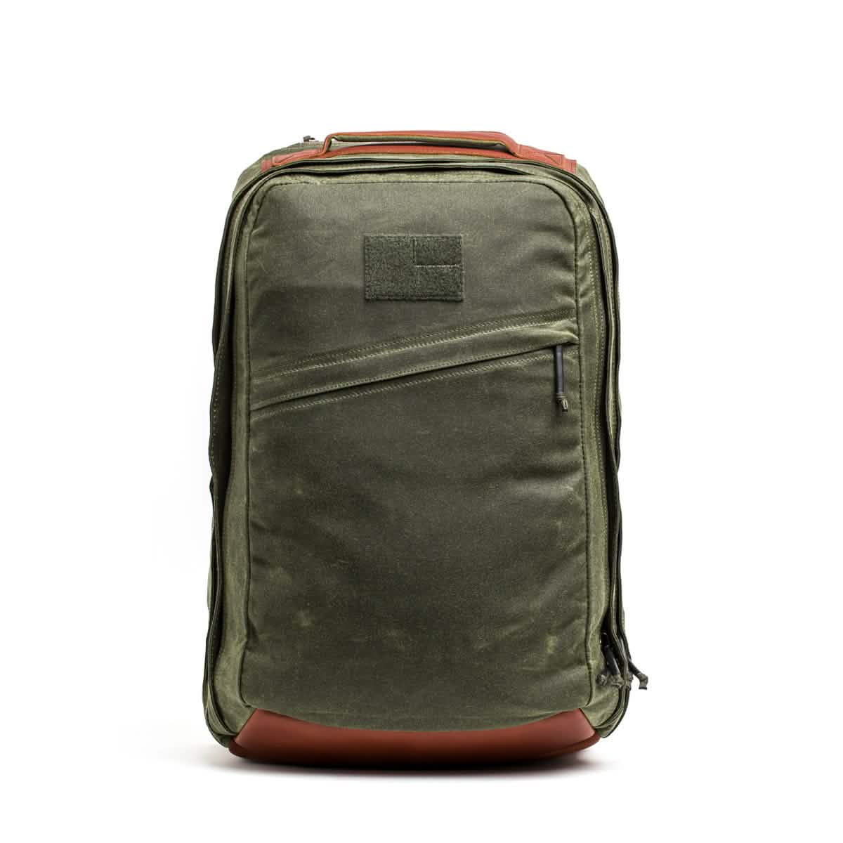 The GR2 - Waxed Canvas by GORUCK showcases a minimalist design in green with brown accents and a front zipper pocket. Made from waxed duck canvas, it stands upright against a white background, featuring a sturdy top handle and adjustable straps for enhanced comfort.