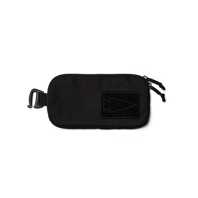 The Sternum Pouch - Cordura by GORUCK is a sleek black rectangular pouch, designed to perfectly fit as a sternum pouch. It features a zipper closure and a convenient carabiner clip on the left side. A distinctive black patch adorned with an outlined arrowhead design enhances the front, offering stylish functionality that seamlessly integrates with your Rucker gear.