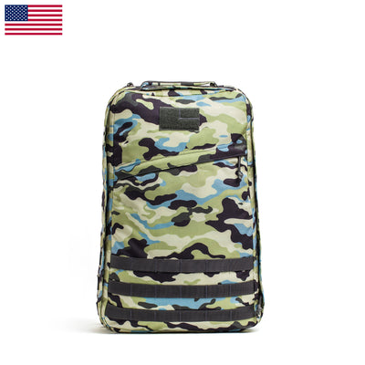 The GR1 USA - Cordura (The Original Ruck) from GORUCK showcases a distinctive camouflage design in green, black, and blue hues, accented by a small United States flag graphic. This Special Forces grade rucksack includes a bombproof laptop compartment for unmatched durability and protection during any adventure.