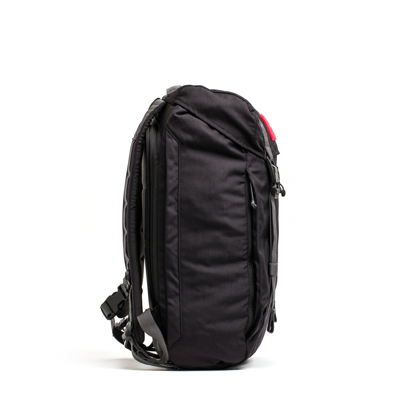 Side view of the GORUCK M23 - Cordura, a modern black backpack made from durable materials, featuring multiple compartments and adjustable straps, set against a white background.