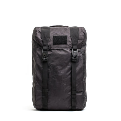 The GORUCK M23 - Dyneema is a black, rectangular, modern rucksack featuring two adjustable straps, a top handle, and a front flap secured by buckles. Made from durable and weather-resistant fabric, it's ideal for outdoor adventures or travel.