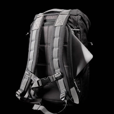 The GORUCK M23 - Cordura, a black backpack crafted from durable materials with gray straps, showcases a visibly secured laptop inside against a dark background.