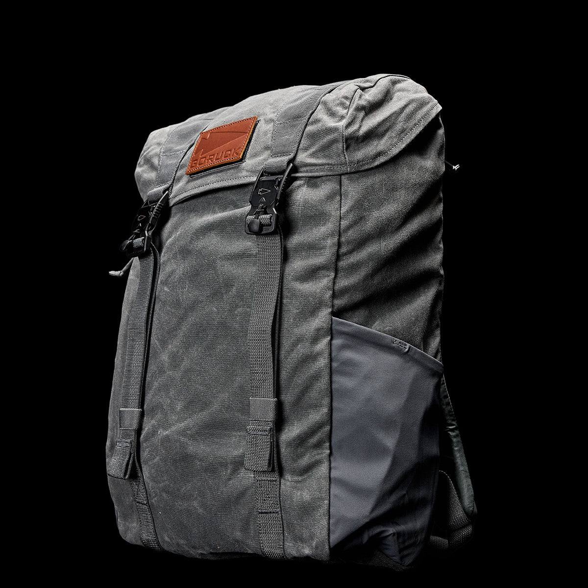 A durable gray M24 rucksack from GORUCK, featuring a waxed canvas material, a leather patch on the flap, adjustable straps, and side pockets is set against a black background.