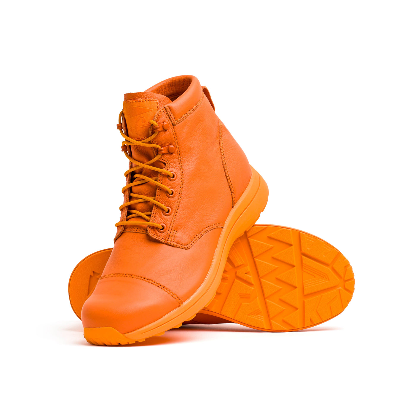 The MACV-1 Traveler x Carryology - Berserker Viking boots by GORUCK are a stylish pair of vibrant orange footwear, with one standing upright and the other lying on its side to highlight the zigzag pattern on the sole. Made from water-resistant leather, these boots feature detailed stitching and matching laces, making them perfect for travel and adventure.