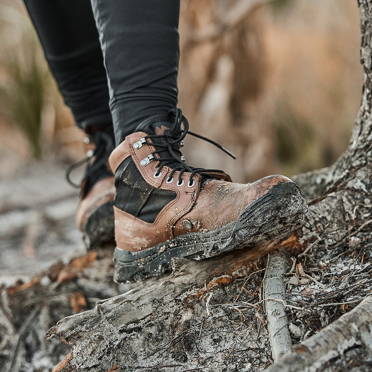 Close-up of someone wearing chestnut and black MACV-2 Mid Top hiking boots with a triple compound outsole, navigating uneven, rocky terrain.