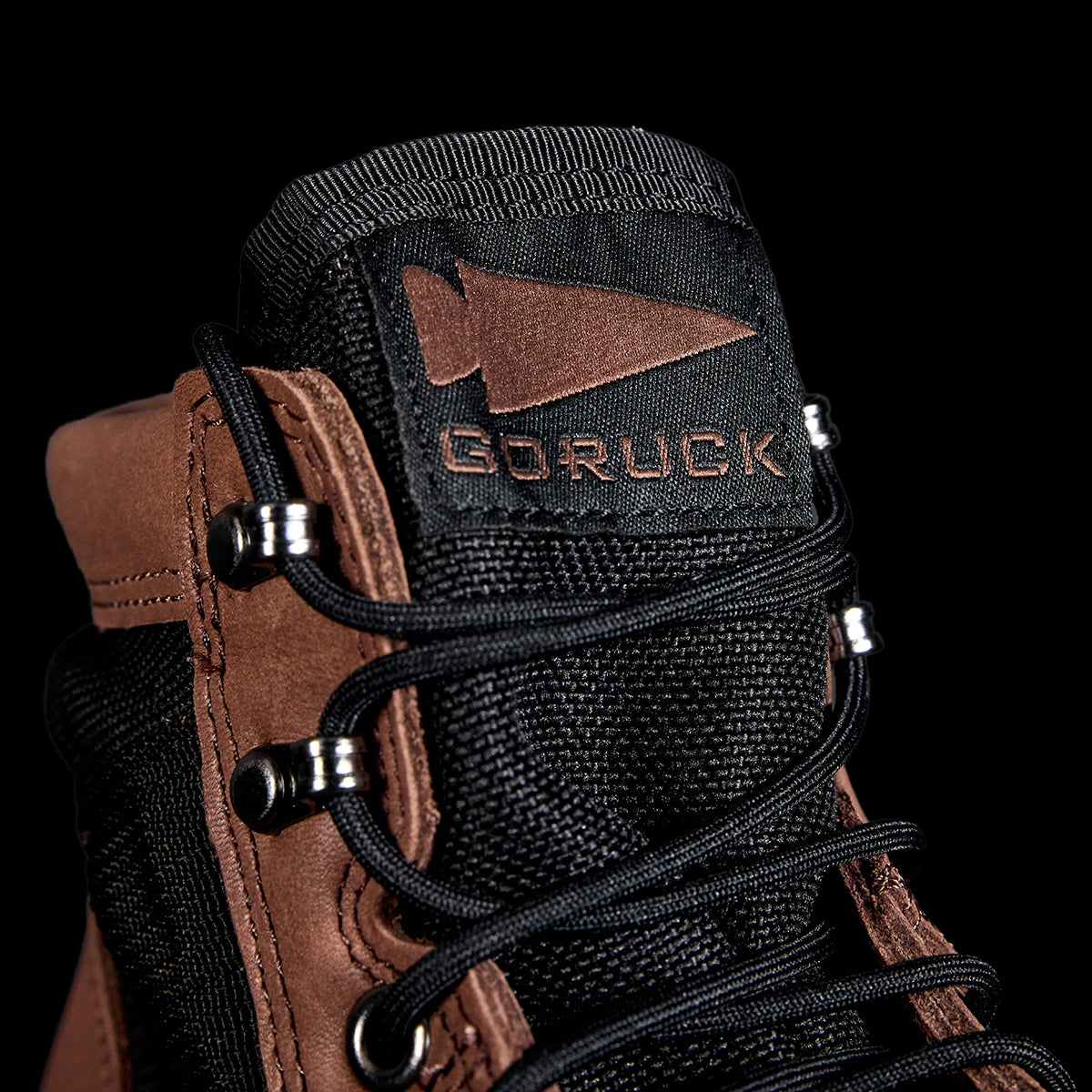 Close-up of a chestnut MACV-2 mid top boot with black laces, logo on the tongue, and a triple compound outsole against a black background.