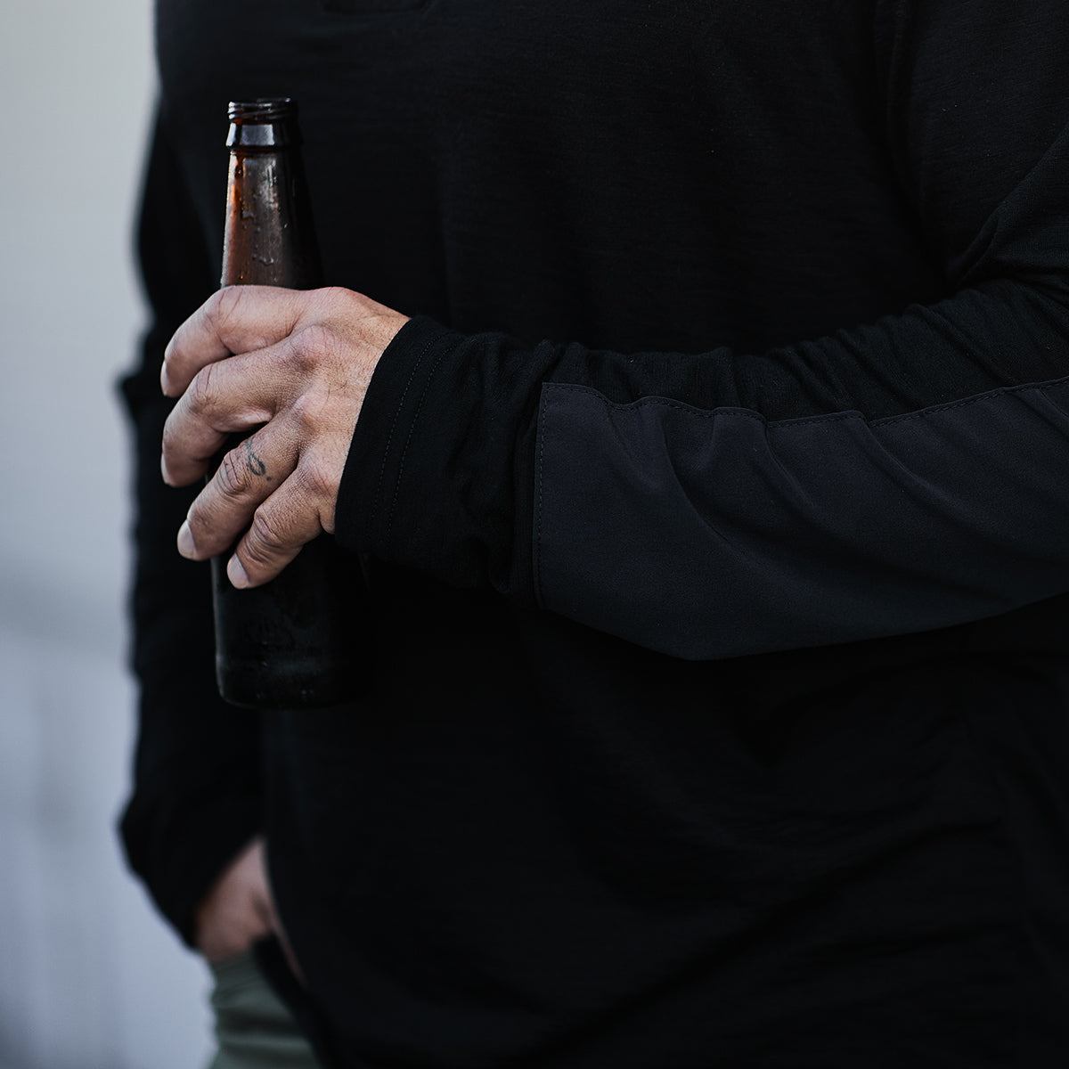 A person wearing the Men’s Commando Long Sleeve by GORUCK, made from merino wool, casually holds a dark beer bottle.