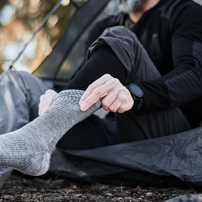 A person outdoors in outdoor gear adjusts their gray breathable Men’s Base Layer Bottom made from merino wool.