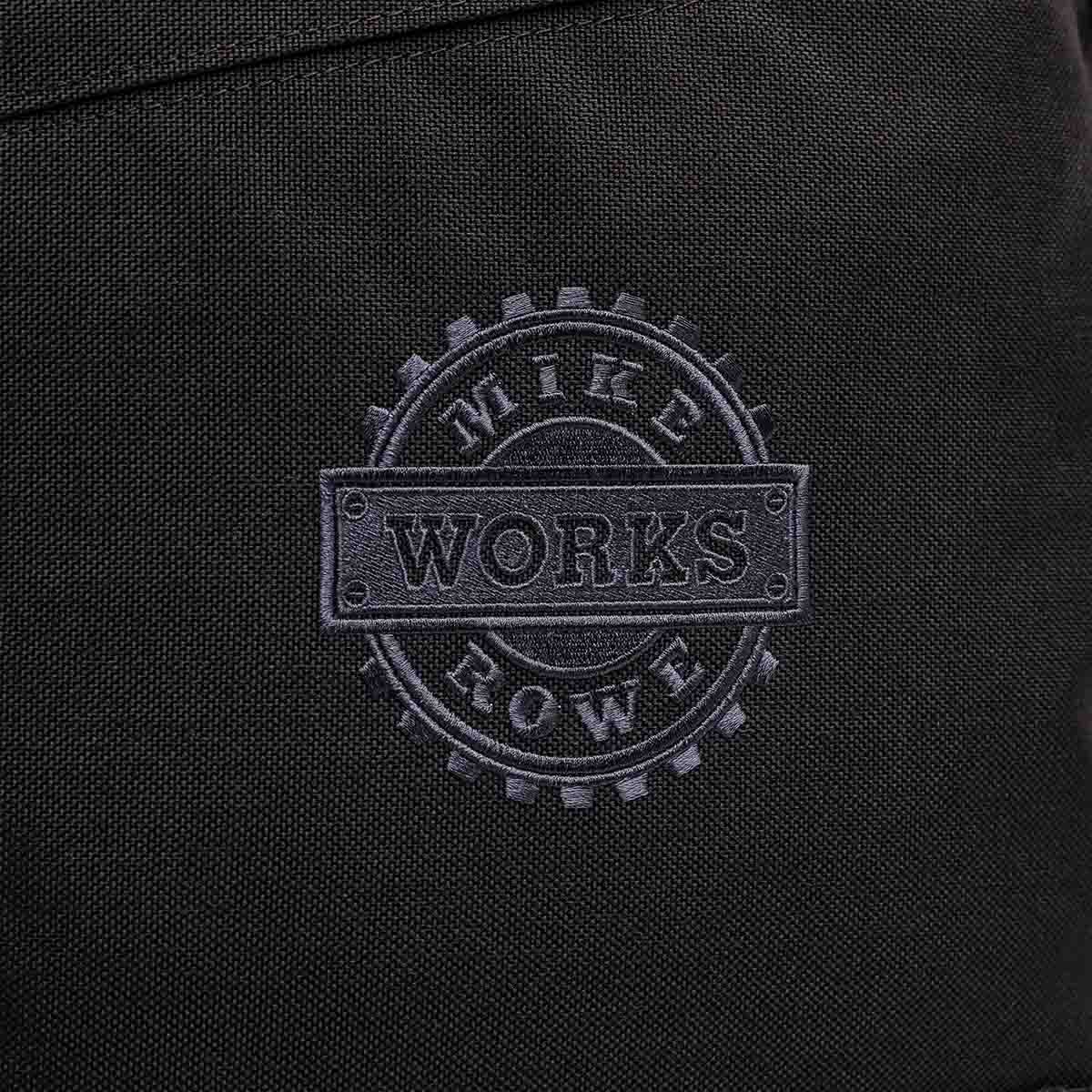 Close-up of black fabric with a gray embossed "WORKS" logo inside a gear design, emblematic of the rugged jobs supported by the GORUCK X mikeroweWORKS Foundation Bundle.