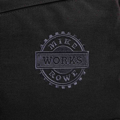 Close-up of black fabric with a gray embossed "WORKS" logo inside a gear design, emblematic of the rugged jobs supported by the GORUCK X mikeroweWORKS Foundation Bundle.