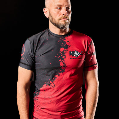 A man wearing the Murder Yoga Rash Guard by GORUCK, featuring a black and red graphic design and made from moisture-wicking comfort material, stands against a black background.