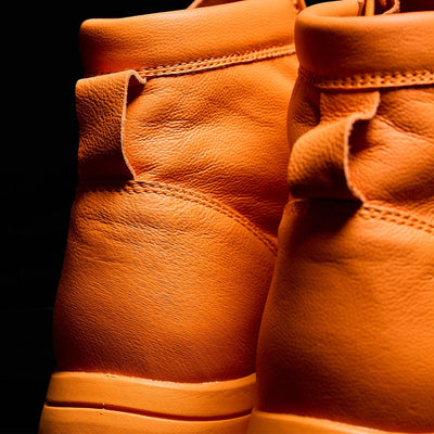 A close-up captures the limited edition MACV-1 Traveler x Carryology - Berserker Viking sneakers by GORUCK, showcasing their vibrant orange leather with textured surfaces against a dark background. The focus is on the back part of the shoes, highlighting intricate stitching details and water-resistant leather.