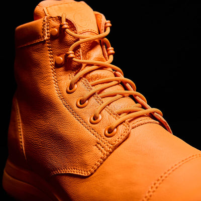 Close-up of an orange limited edition leather boot, the MACV-1 Traveler x Carryology - Berserker Viking by GORUCK, featuring detailed stitching and laces, set against a dark background.