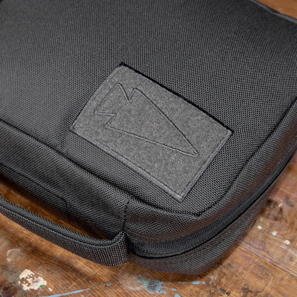 Close-up of the black textured GR2 Field Pocket, crafted from durable 1000D Cordura with an abstract patch, on a wooden surface.