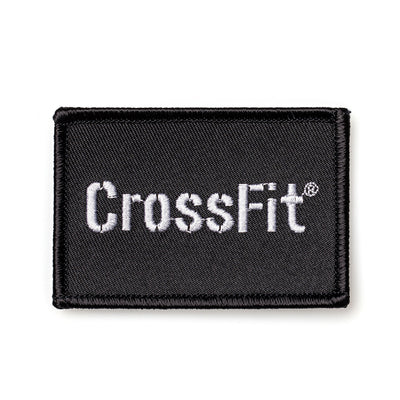 The Patch - GORUCK x CrossFit is a black rectangular patch featuring "CrossFit" in white, with a velcro backing for easy attachment. This durable accessory, inspired by GORUCK challenges, is perfect for showcasing your dedication on any gear.