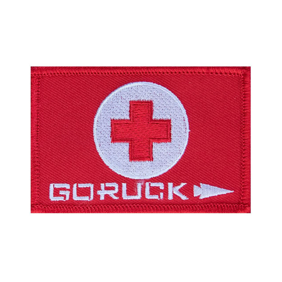 The Patch - GORUCK First Aid features a red design with a white cross in a circle and "GORUCK" text with an arrow, ideal for attaching to pouches or carrying essential medical supplies.