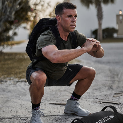 A man doing squats outdoors is enhancing his workout with the Rucker 4.0 weighted rucksack, embracing the art of rucking.