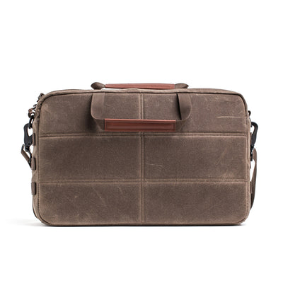 The GORUCK Shoulder Bag - Waxed Canvas is a brown canvas laptop bag with a Martexin Wax finish and leather accents. It features an asymmetrical design for versatile carrying and is showcased against a plain white background for a sleek appearance.