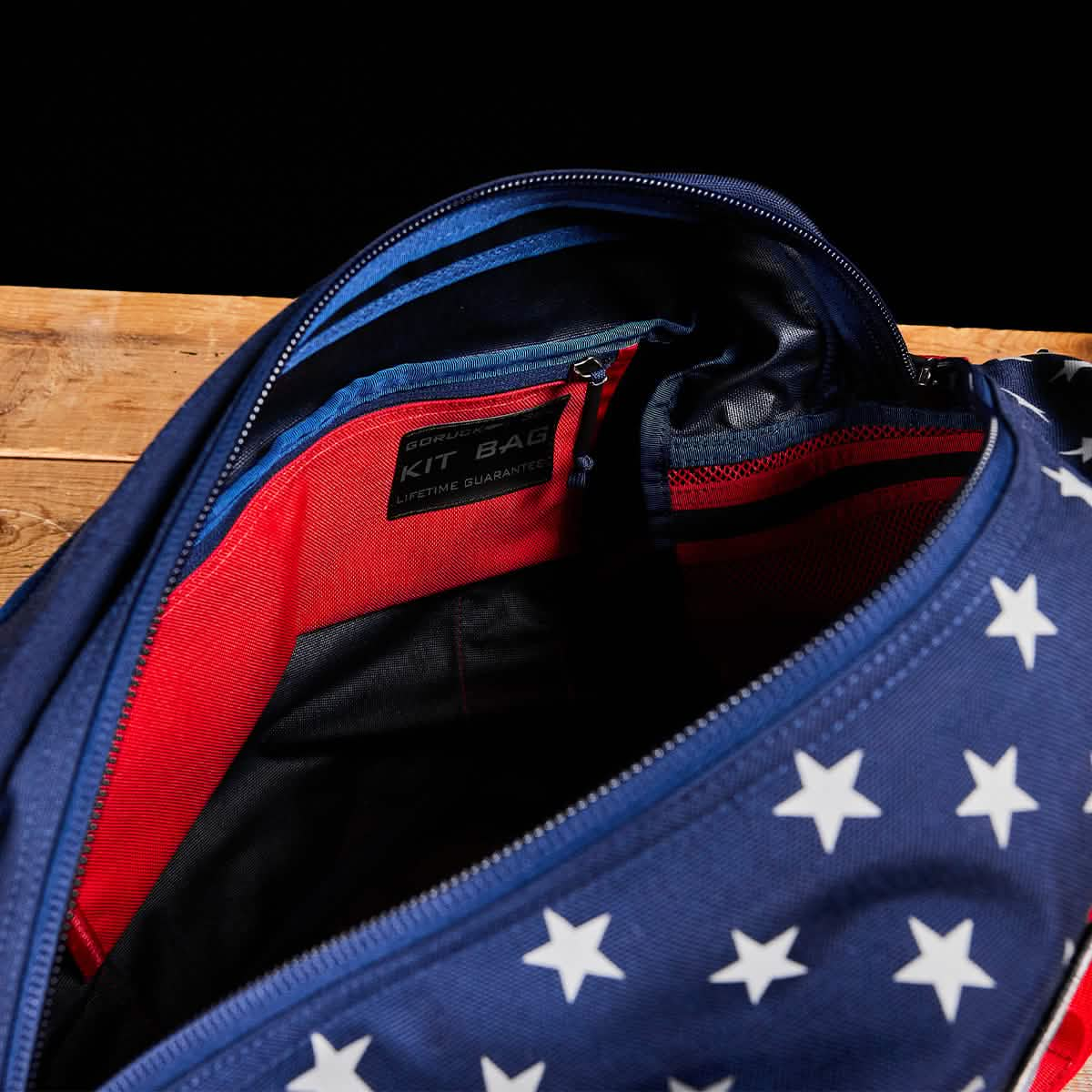 A Kit Bag (includes shoulder strap) with a stars-and-stripes design rests on a wooden surface, its label clearly displaying "kit bag.