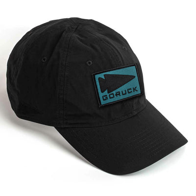 The Performance TAC Hat - TOUGHDRY w/Patch is a black baseball cap with a teal arrowhead logo and "GORUCK" on a patch. Made from ToughDry fabric, it features patch-friendly VELCRO for customization.