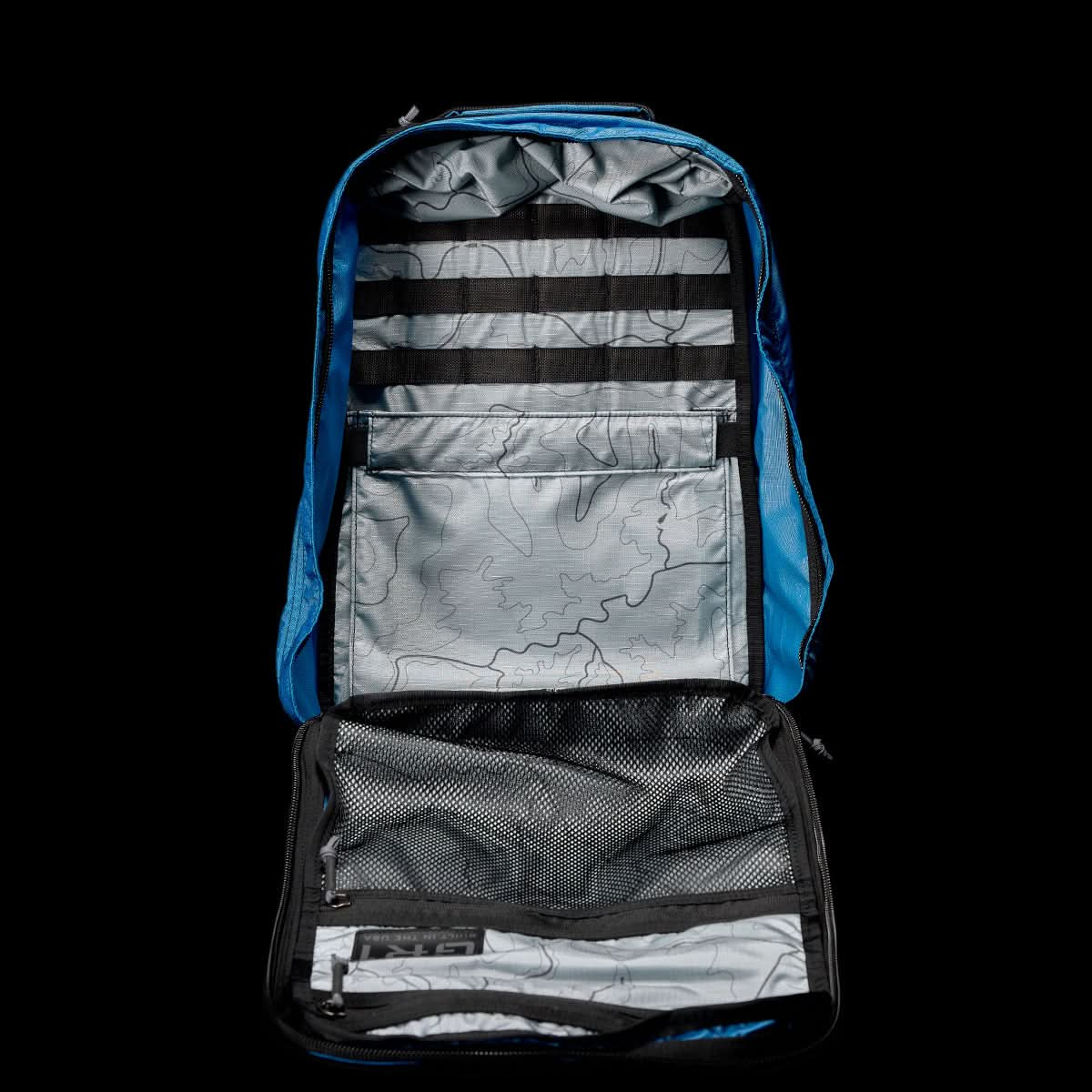 Display the GR1 USA - Ripstop ROBIC®, a blue, ultra-lightweight rucksack by GORUCK, on a black background, highlighting its interior compartments with a mesh pocket and map-patterned lining.