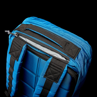 Close-up of the GORUCK GR1 USA - Ripstop ROBIC® backpack in blue, crafted from water-resistant materials, featuring black straps and a small zippered pocket set against a black background.