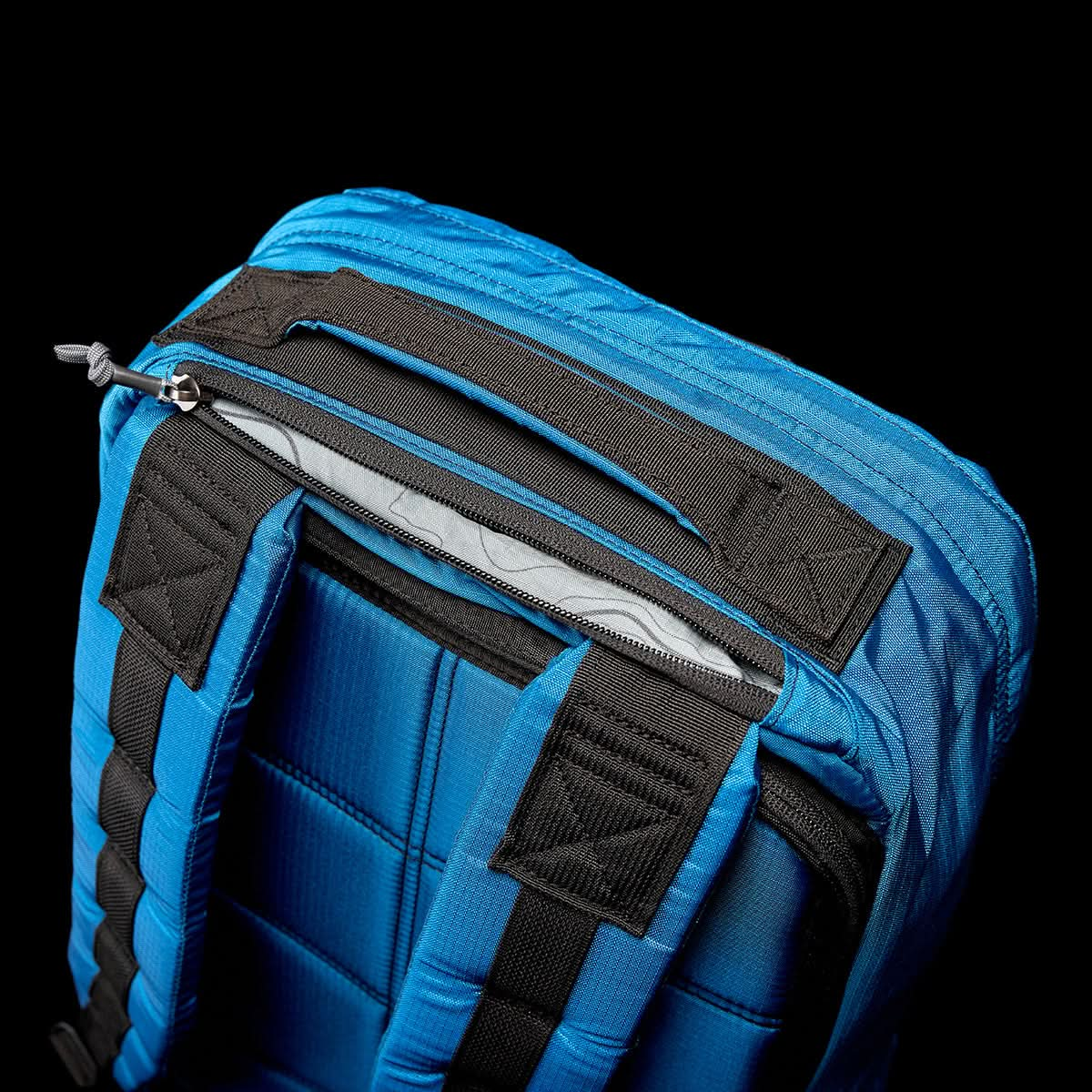 Close-up of the GR1 USA - Ripstop ROBIC® by GORUCK, featuring a blue, ultra-lightweight design with black straps and a zippered pocket against a dark, water-resistant background.