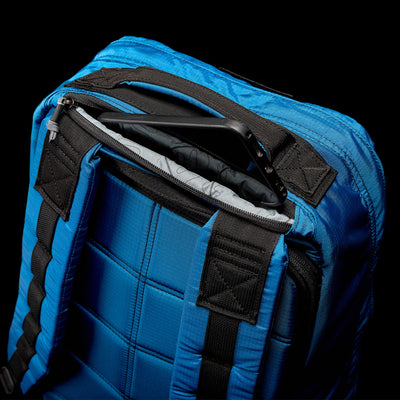 The GR1 USA - Ripstop ROBIC® backpack by GORUCK, in blue with an ultra-lightweight quilted pattern, sits partially open to reveal a tablet inside against a black background.