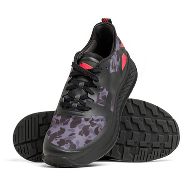 The Women's Rough Runner by GORUCK in Midnight Frogskin and High Risk Red features a pair of athletic shoes with a black base, showcasing a gray camouflage pattern and striking red accents. One shoe stands upright while the other leans against it, highlighting the detailed tread pattern crafted for tough terrains. The shoes come equipped with an EVA midsole for optimal comfort and performance.