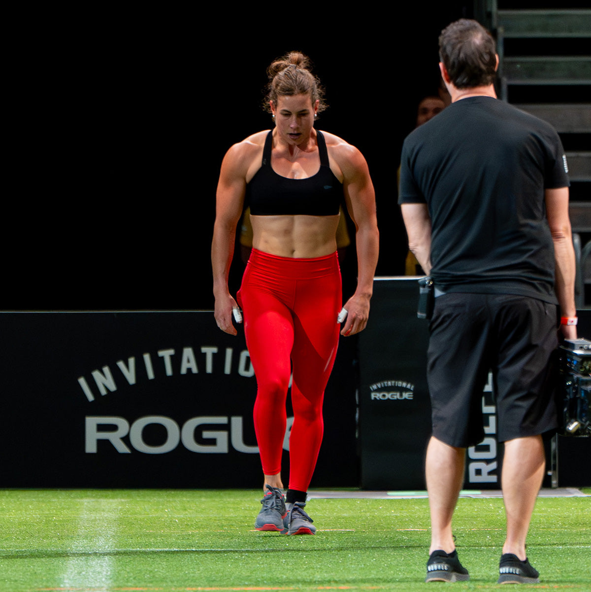 An athlete in a sports bra and vibrant red Women’s Training Leggings Pocket - ToughFlex prepares intensely on the grassy field, embodying the spirit of a GORUCK Challenge.