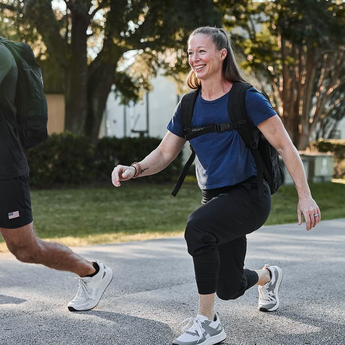 Woman exercising outdoors, wearing Women's Performance Joggers and Rucker 4.0. She is performing lunges on a sidewalk surrounded by trees and grass.