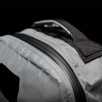 Close-up of the GR1 USA - X-PAC by GORUCK, featuring its gray textured X-PAC fabric and black zipper. The visible top handle stands out against the dark background, emphasizing its waterproof design.