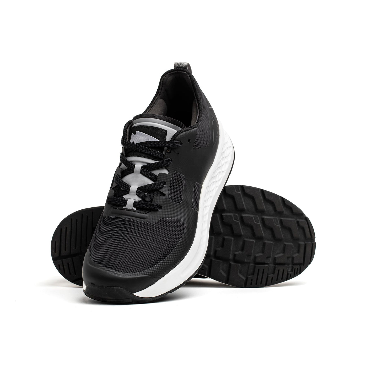 Introducing the Women's Rough Runner - Black + White by GORUCK, a pair of athletic shoes that boasts an innovative Gradient Density™ technology for enhanced comfort. Featuring white soles and a textured sole pattern, one shoe stands upright while the other leans against it. The sleek black design with matching laces is ideal for any adventure.